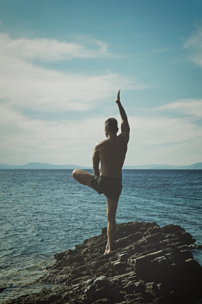 services-01 Back view of a man practicing yoga on a rocky seashore. Embracing peace, meditation, and nature.
